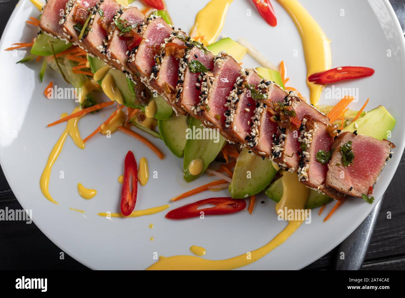 Cuisine japonaise. Tatataki avec thon. Poisson frit avec graines de sésame et sauce soja, wasabi, citron vert. Sur un oreiller de légumes. Avocats, bandes de piment Banque D'Images