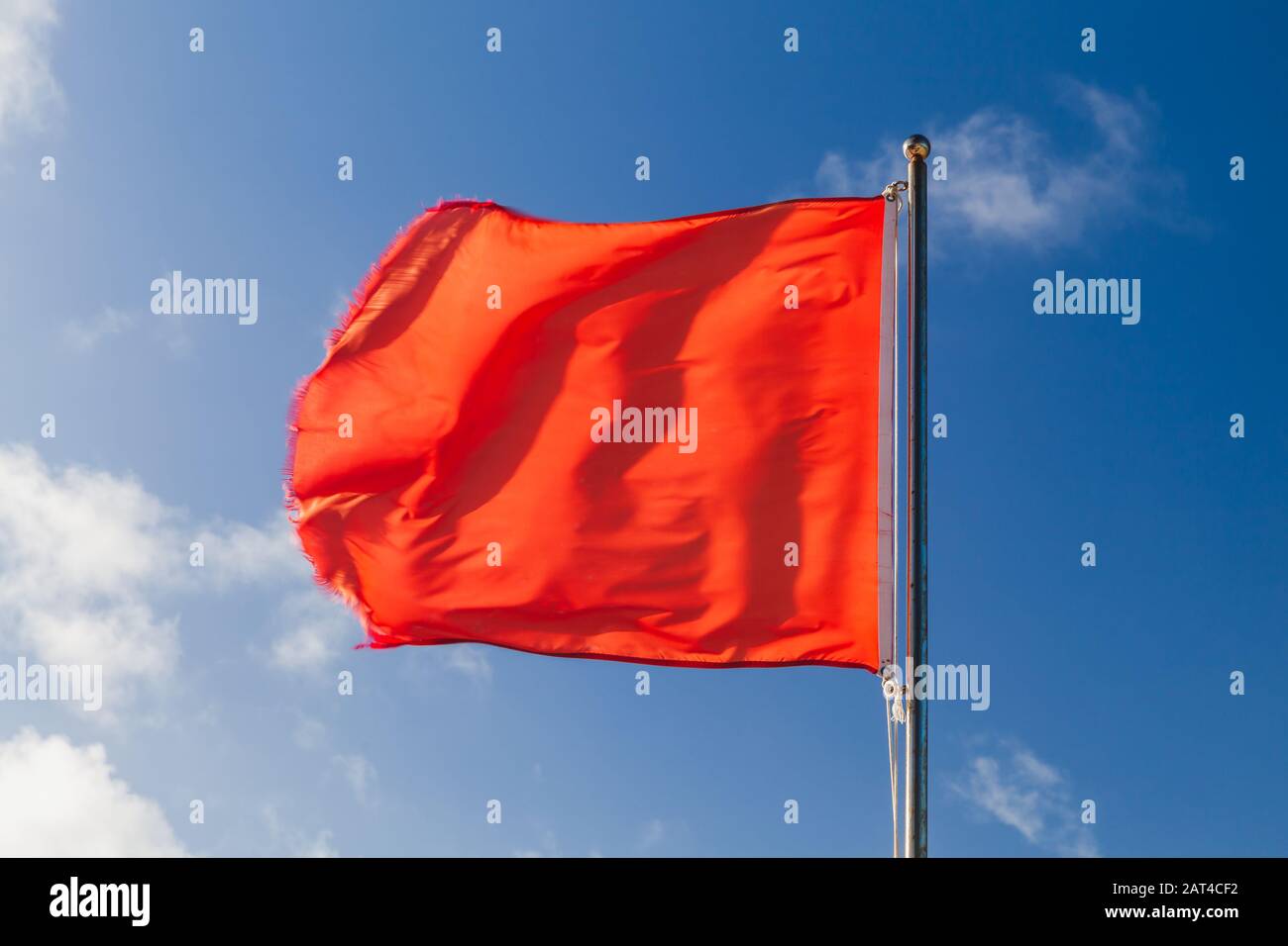 Drapeau d'avertissement rouge sur une plage agitant sur le vent fort au-dessus du ciel bleu Banque D'Images
