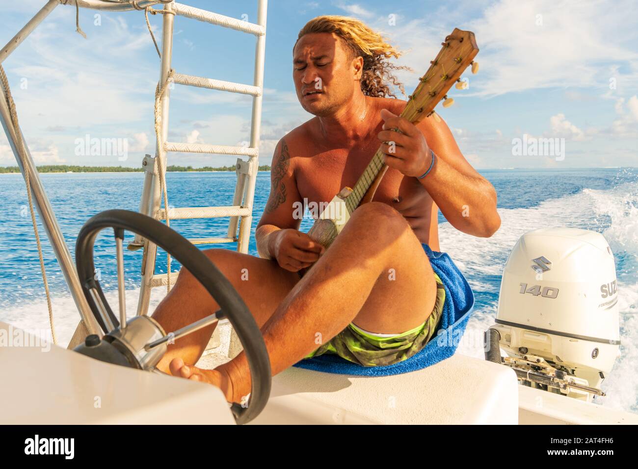 L'homme polynésien dirige un bateau avec son pied tout en jouant à l'ukulele. Banque D'Images