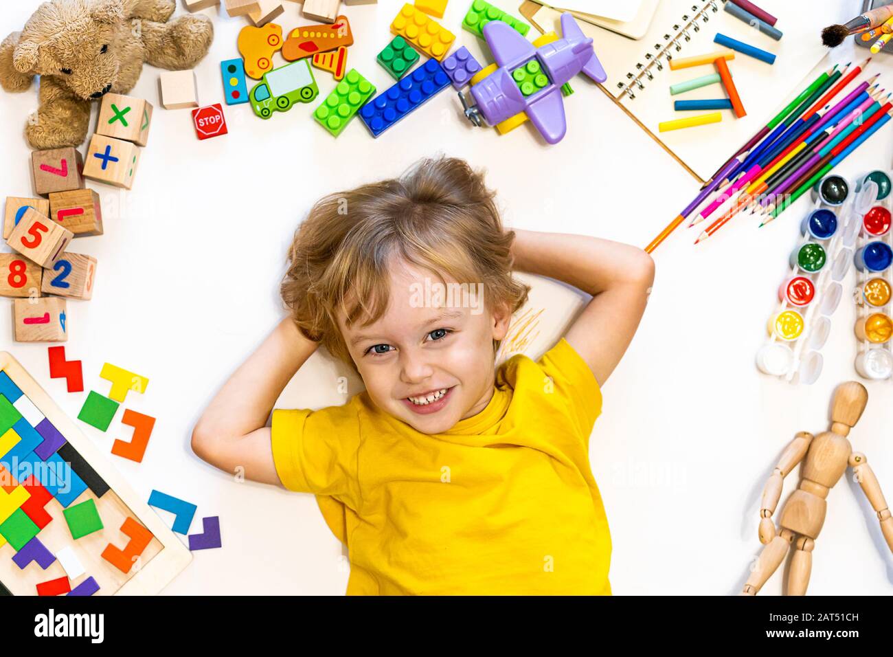 Joli garçon souriant et plein de style, plein de blocs, d'avions et de voitures. Jouets éducatifs et fournitures scolaires pour la maternelle et la maternelle. Enfant à la maison ou en garderie. Vue de dessus Banque D'Images