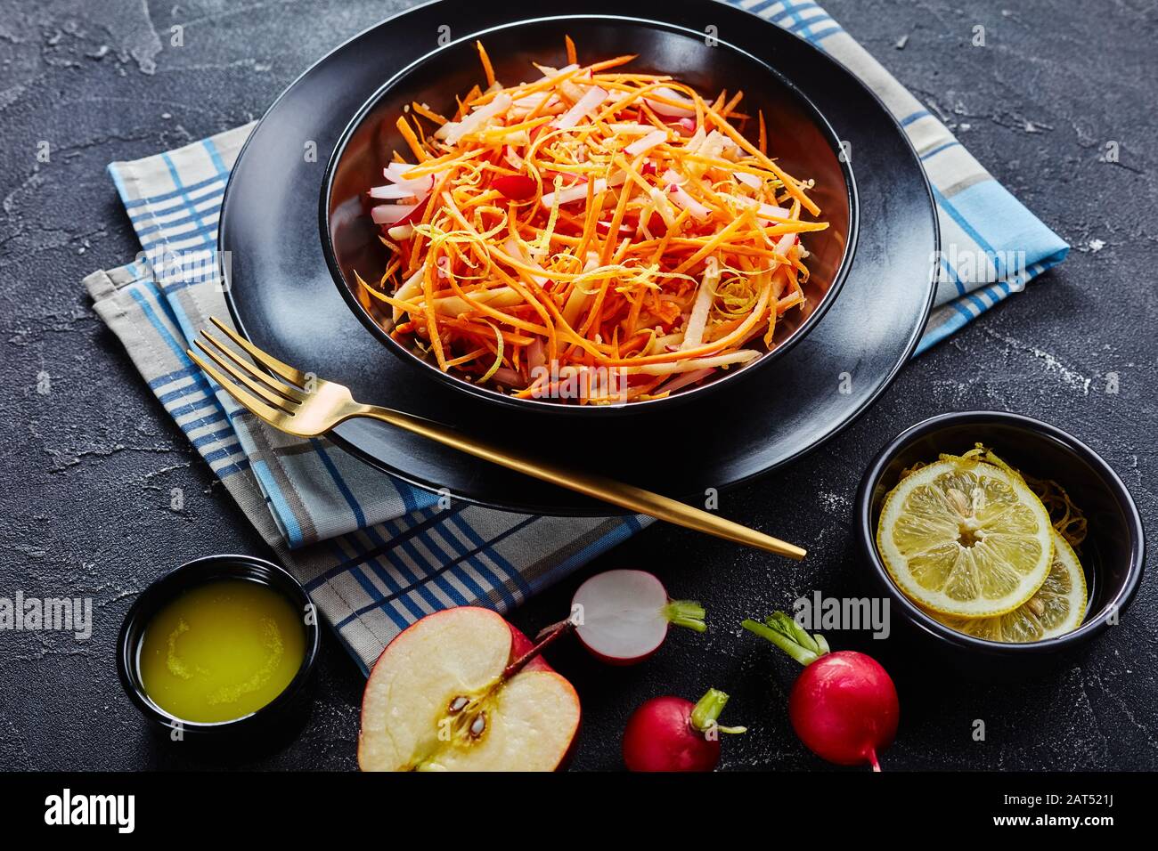 Gros plan de raifort Frais de carottes et salade de pommes parsemées de graines de quinoa et de zeste de citron dans un bol noir sur une table en bois avec vinaigrette maison Banque D'Images