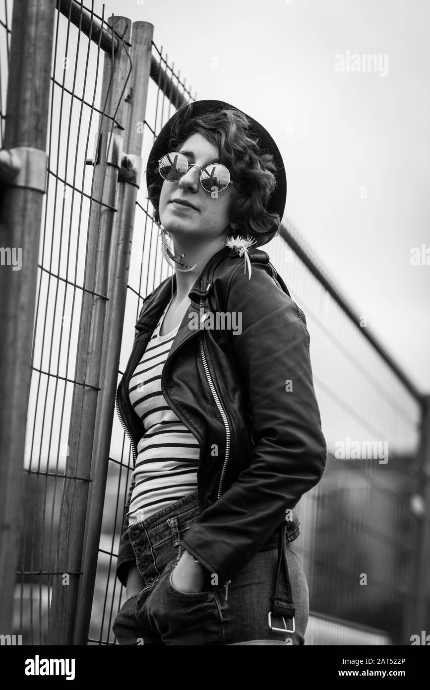 Portrait d'une jeune fille de vingt ans avec une veste en cuir noir posant dans un environnement industriel urbex Banque D'Images