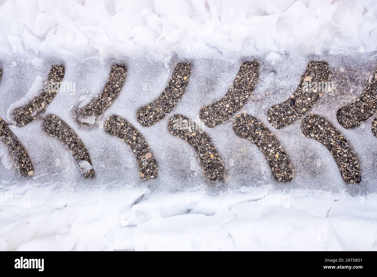 Traces d'un pneu de tracteur sur de l'asphalte neigeux sur une route en hiver. Banque D'Images