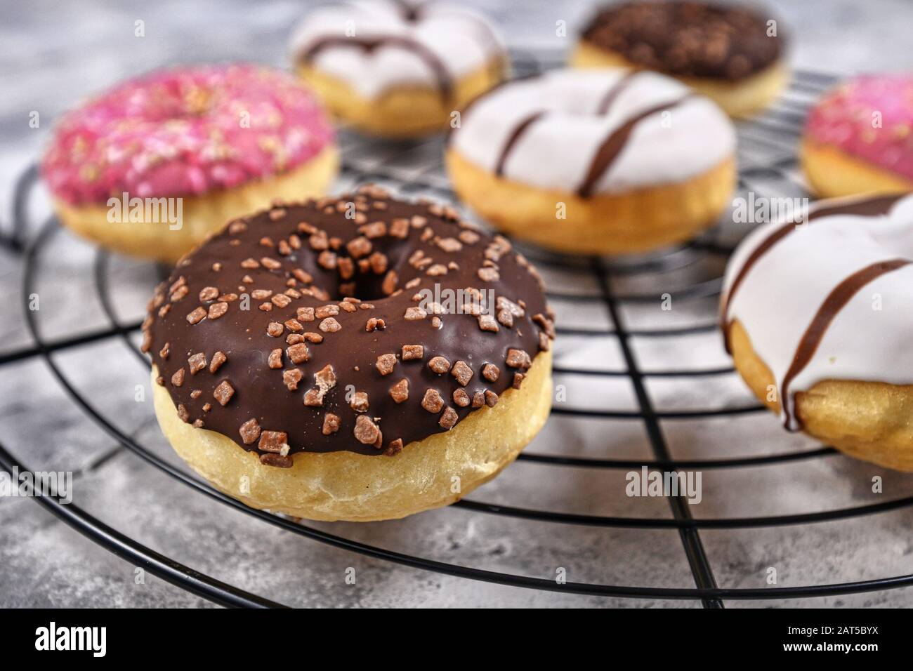 Boulangerie savoureux avec anneau chocolat brun et saupoudre de vitrage sur grille à gâteau avec d'autres donuts colorés en arrière-plan Banque D'Images