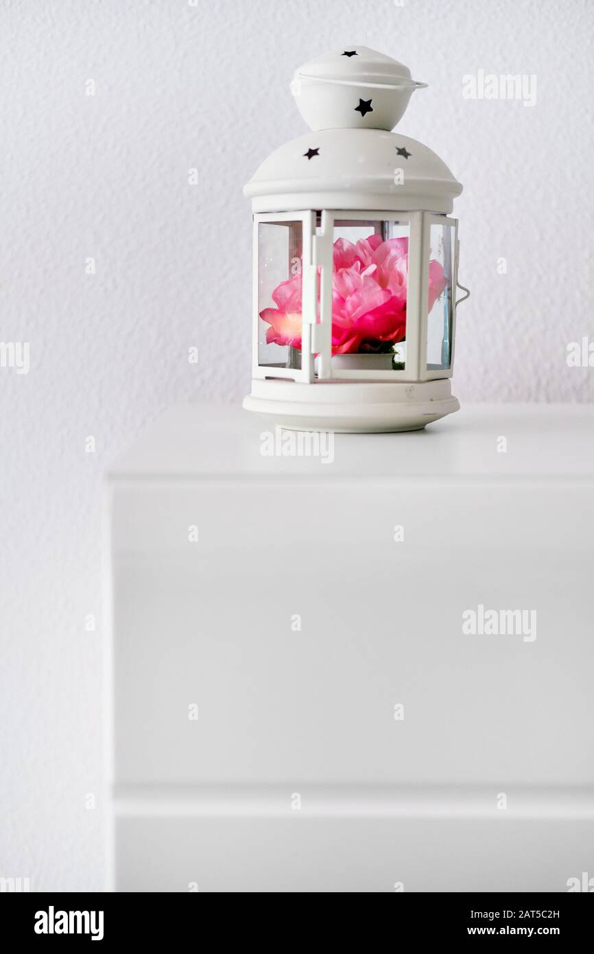 Forme de lanterne en forme de chandelier décorée de supports de fleurs  artificielles roses sur une table de chevet ou une table de nuit contre un  mur de couleur blanche, aucune personne