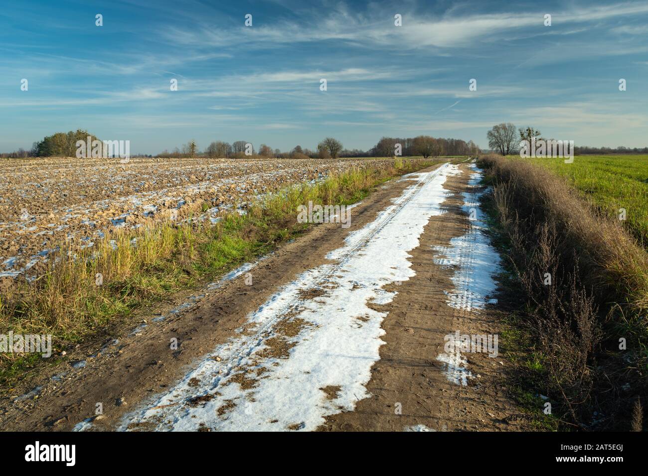 Neige sur une route de terre à travers les champs, l'horizon et les nuages sur un ciel bleu Banque D'Images