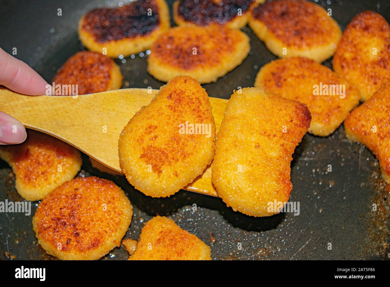 Une main avec une spatule en bois retourne sur la friture des pépites de poulet dans une poêle à frire. Gros plan Banque D'Images