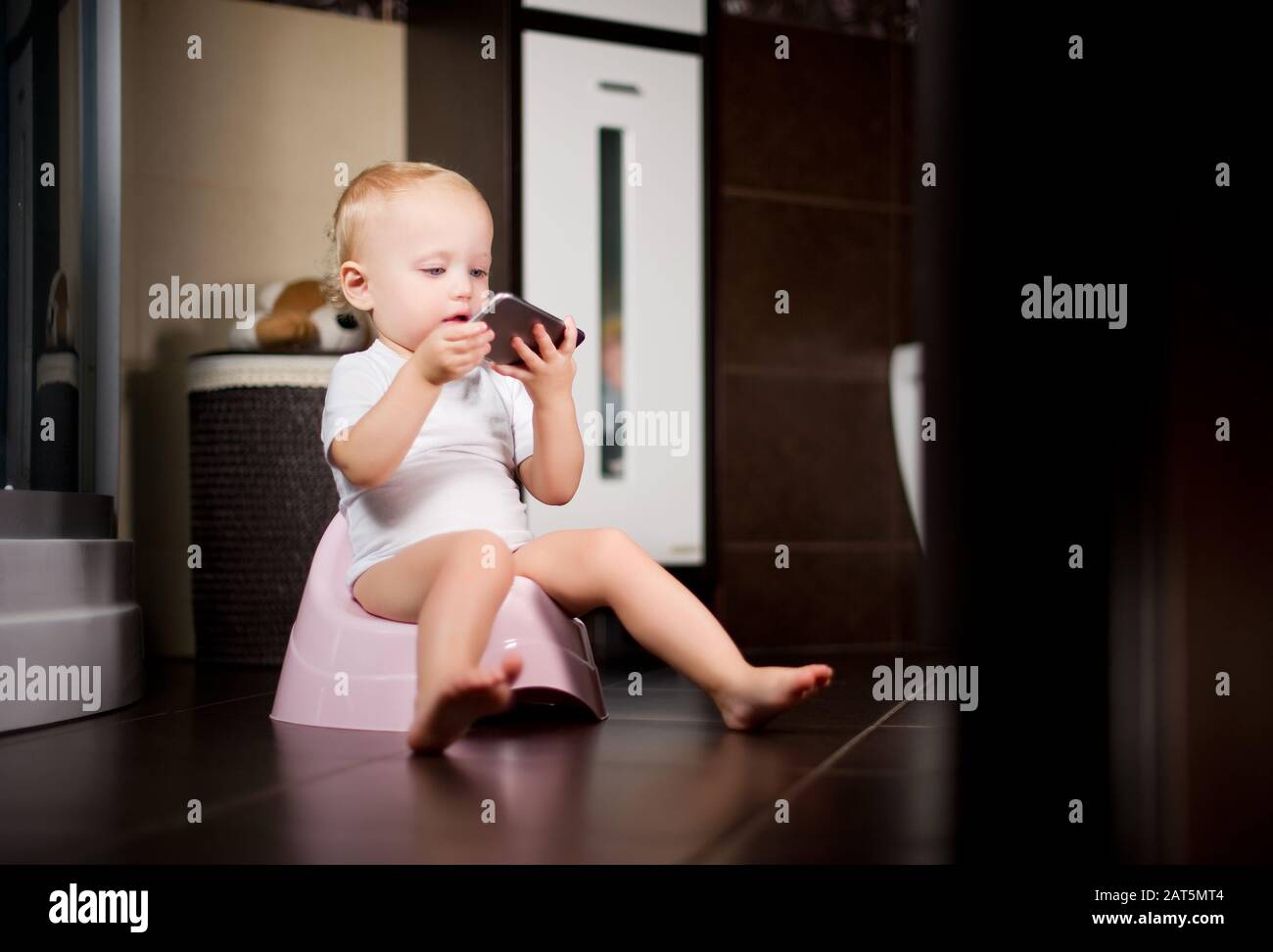 l'enfant tient un smartphone dans ses mains assis sur un pot dans la salle de bains. Tons Banque D'Images