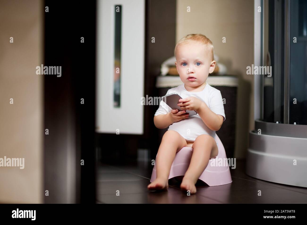 l'enfant tient un smartphone dans ses mains assis sur un pot dans la salle de bains. Tons Banque D'Images