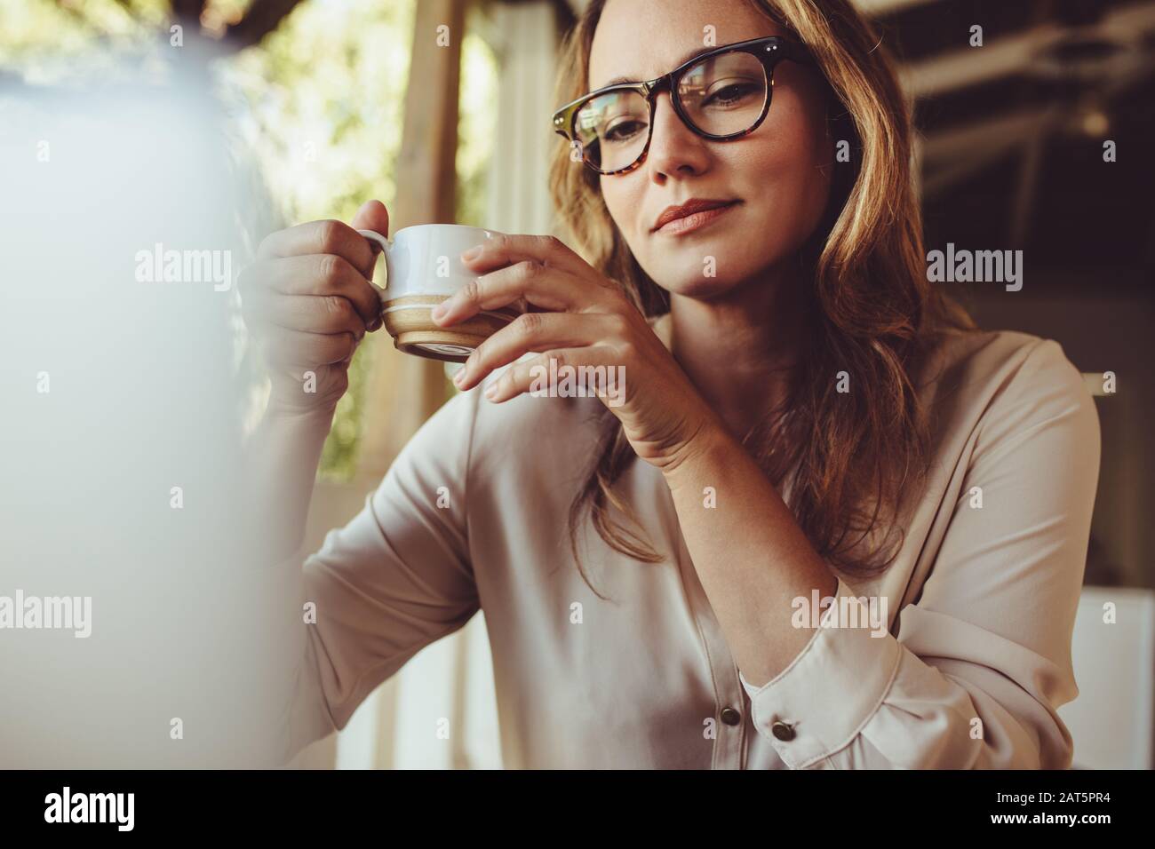 Femme assise au café avec une tasse de café et regardant l'ordinateur portable. Femme d'affaires ayant un café tout en travaillant à partir d'un café. Banque D'Images