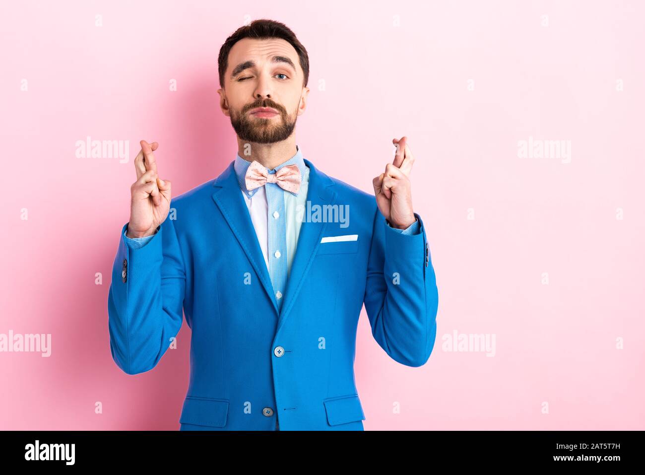 homme barbu en costume avec des doigts croisés qui s'enroulent l'œil sur le rose Banque D'Images