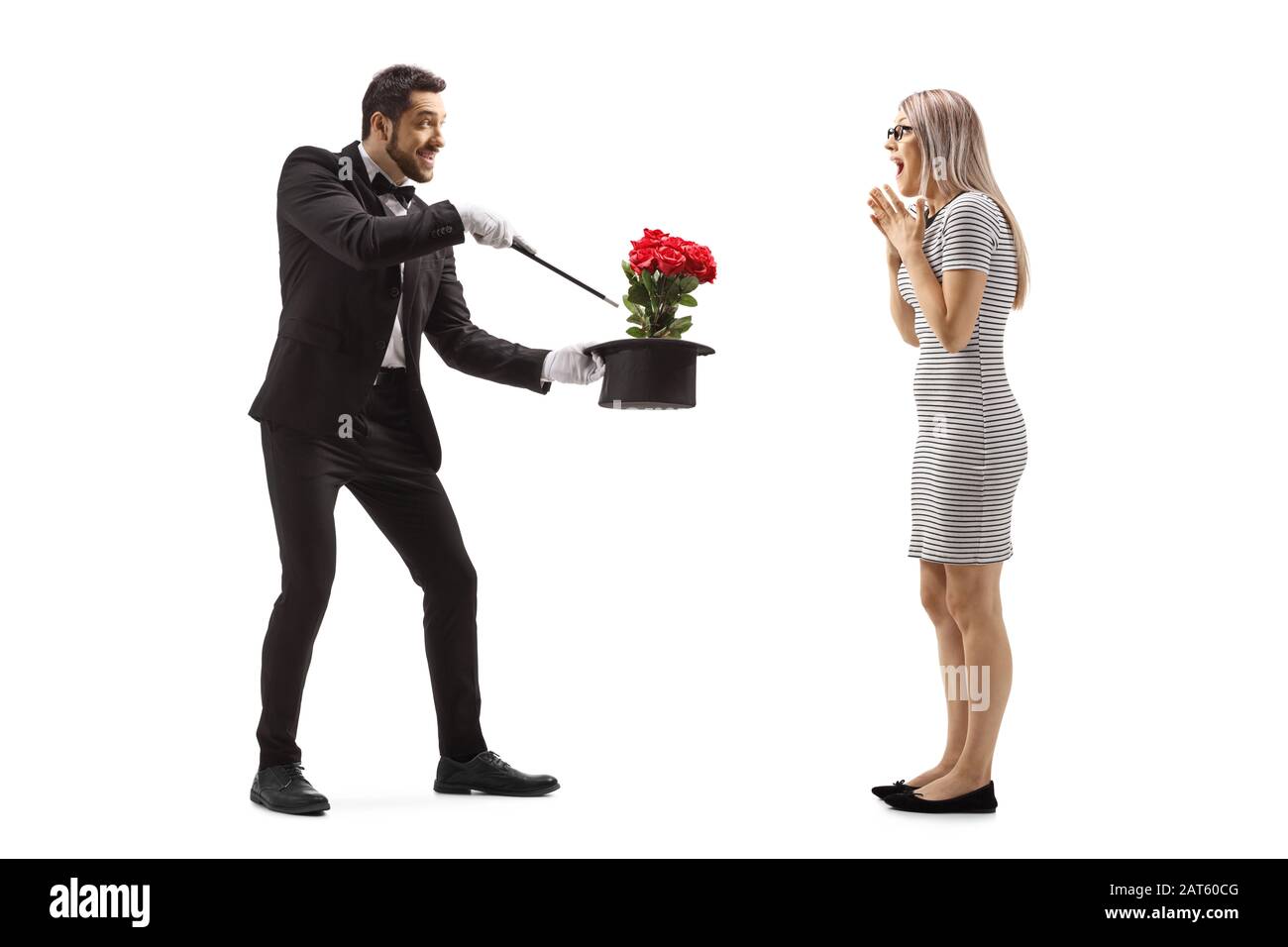 Photo pleine longueur d'un magicien faisant un tour magique avec des fleurs et un chapeau devant une jeune femme surprise isolée sur fond blanc Banque D'Images