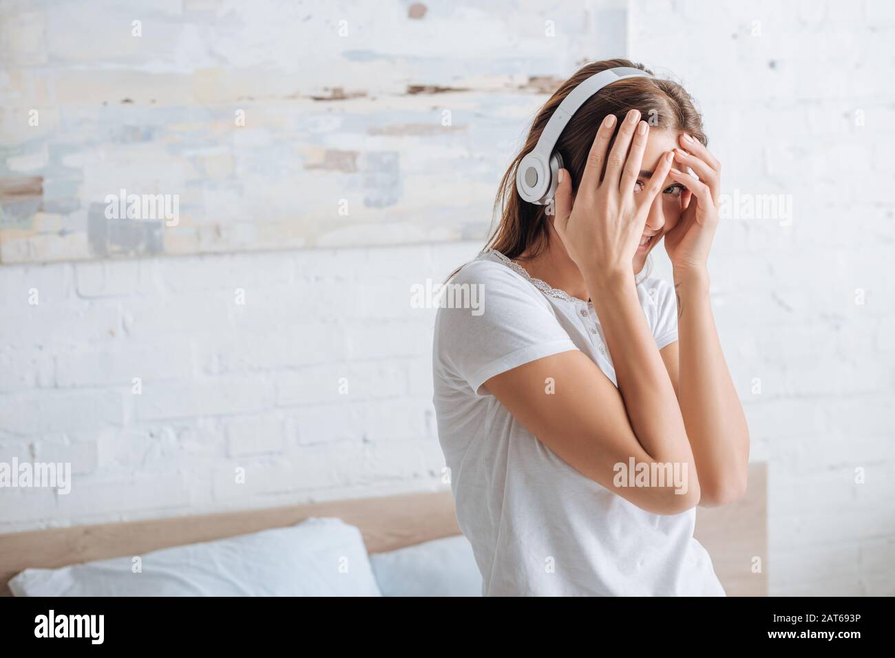 une femme gaie qui couvre le visage tout en souriant et en écoutant de la musique à la maison Banque D'Images