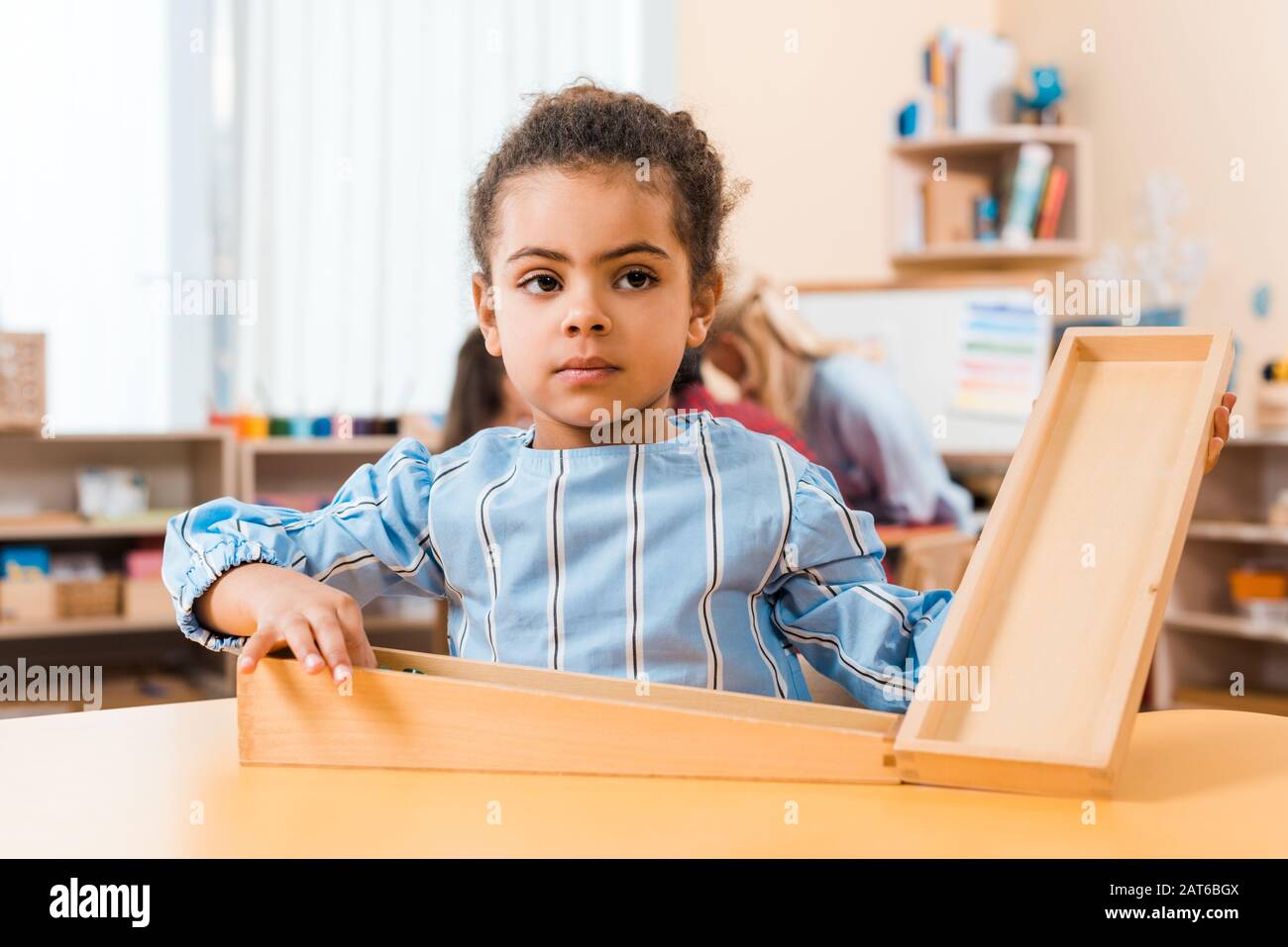 Foyer sélectif de l'enfant africain américain avec jeu en bois et professeur avec des enfants en arrière-plan à l'école de montessori Banque D'Images