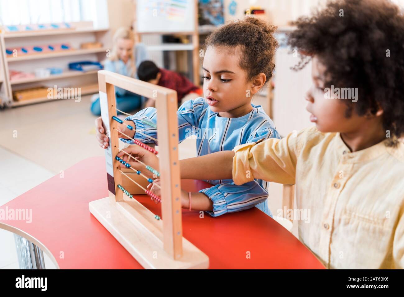 Foyer sélectif des enfants africains américains jouant avec des scores avec enseignant et enfant en arrière-plan à l'école de montessori Banque D'Images