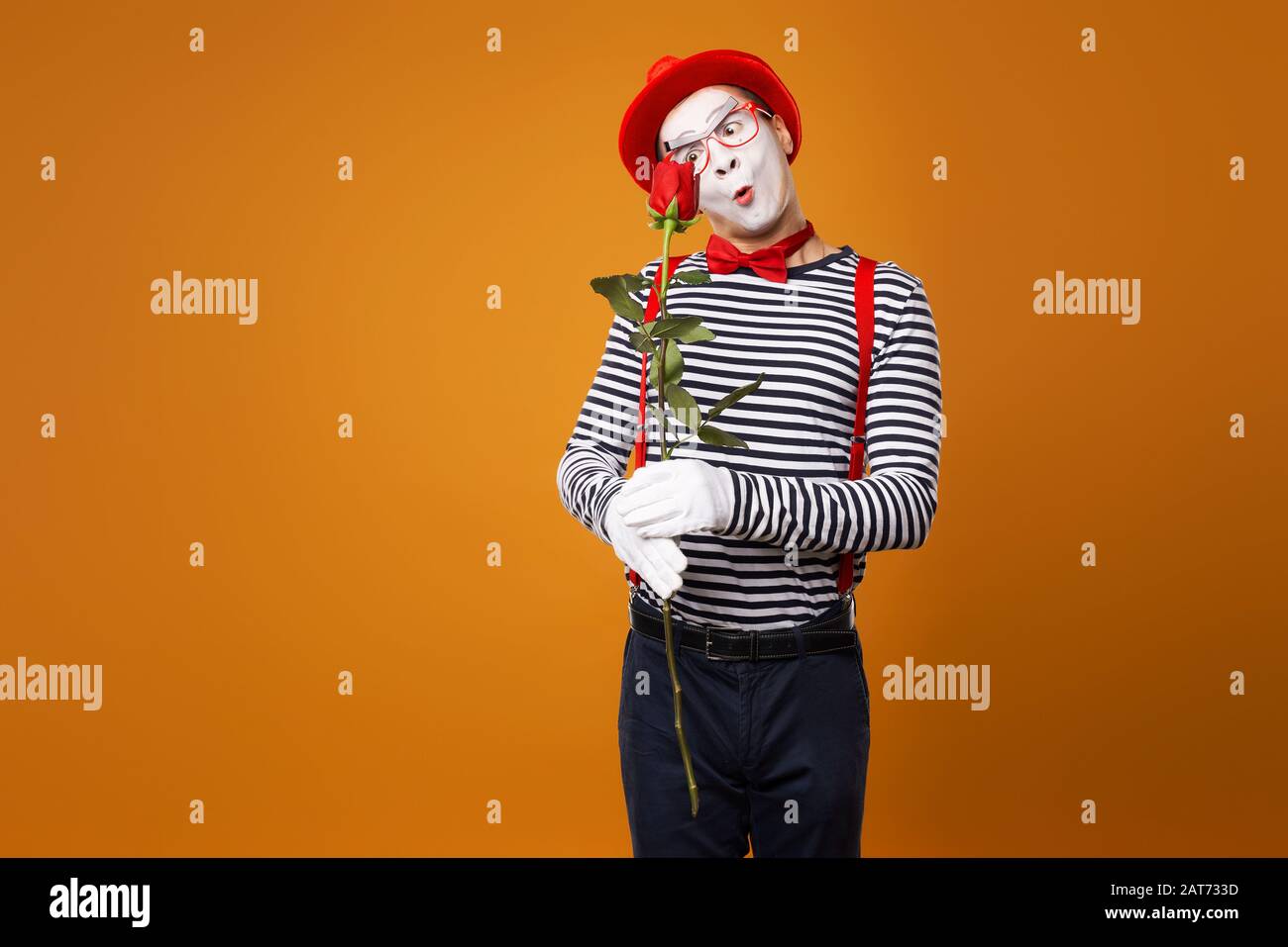 Mécontent du visage blanc dans Red Hat et t-shirt rayé tenant rose sur fond orange vide en studio Banque D'Images