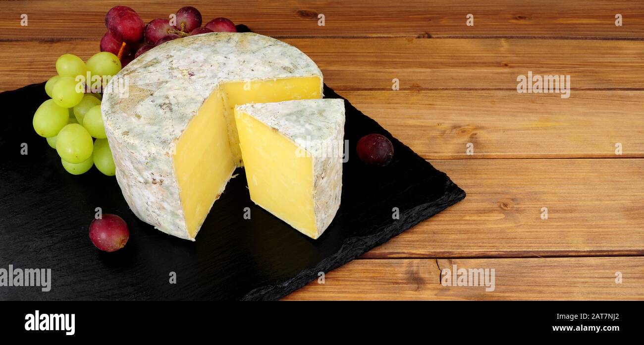 Cave ancienne ferme cheddar fromage sur une planche en ardoise avec un fond en bois Banque D'Images