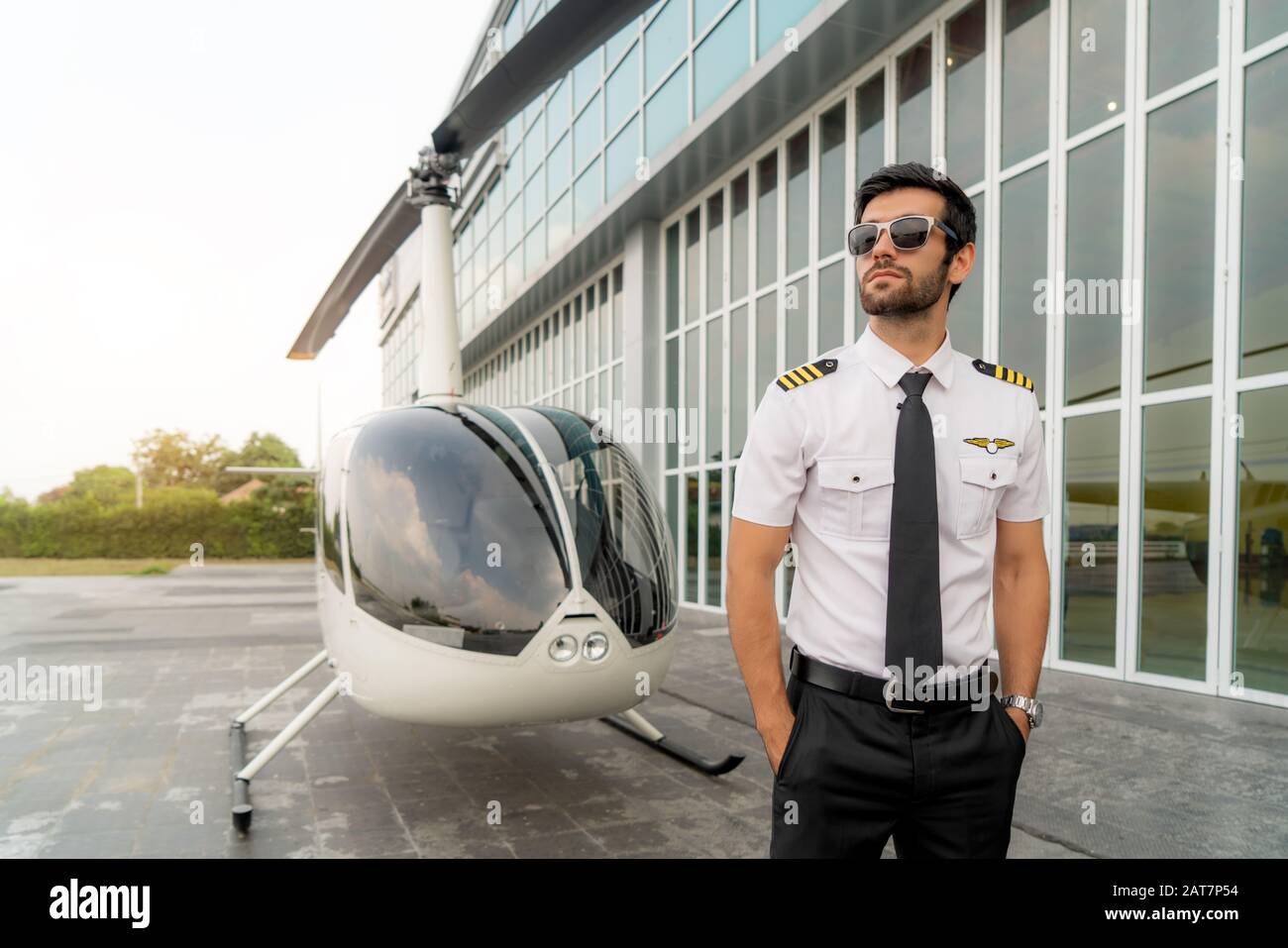 Portrait de beau pilote commercial en uniforme blanc capitaine debout et  regardant intelligent près d'un petit hélicoptère privé sur un point  d'atterrissage avec privé Photo Stock - Alamy