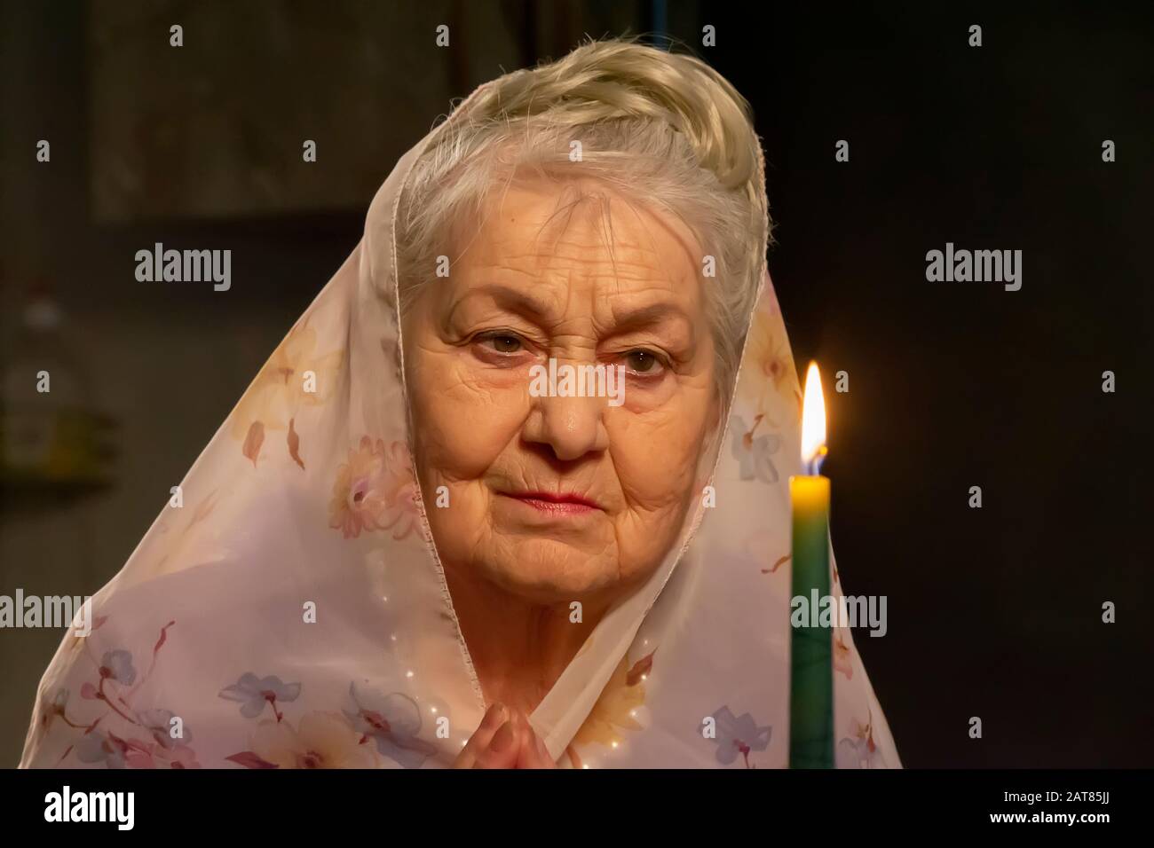 Une femme âgée dans un foulard regarde une bougie.Une femme âgée regarde une bougie. La vieille femme priait. Banque D'Images
