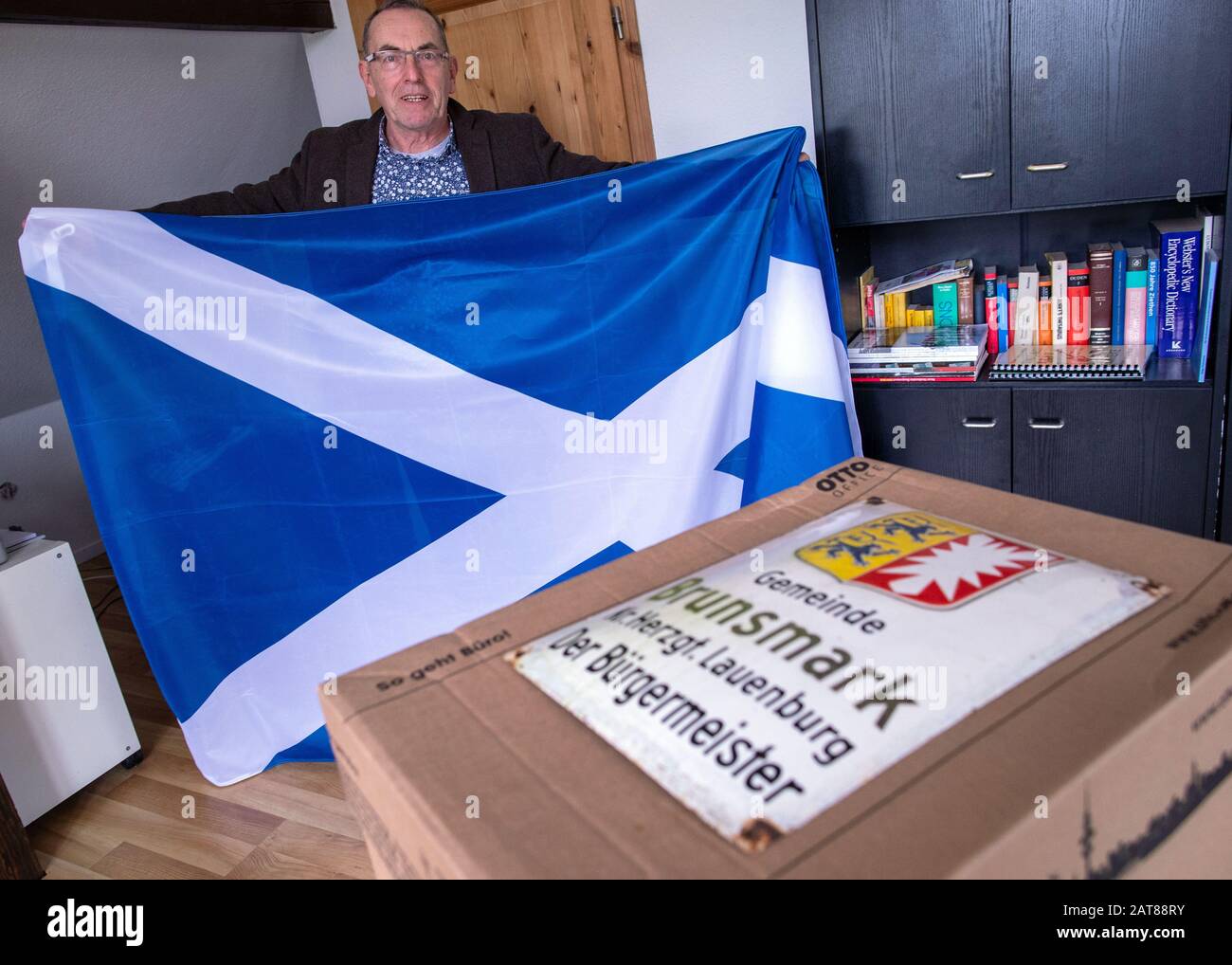 Brunsmark, Allemagne. 31 janvier 2020. Iain Macnab, maire de la petite communauté de Brunsmark près de Mölln, montre un drapeau de l'Ecosse sur son dernier jour de travail, qu'il a reçu comme cadeau d'adieu. Sur le bureau il y a une boîte remplie de documents et le vieux signe du maire de la ville. L'Écosse vit en Allemagne depuis plus de quarante ans et est maire de la ville de 160 habitants depuis onze ans. Avec la brexite Macnab doit démissionner de son bureau en tant que maire et n'est plus autorisé à participer au conseil municipal. Crédit: Jens Büttner/Dpa-Zentralbild/Dpa/Alay Live News Banque D'Images