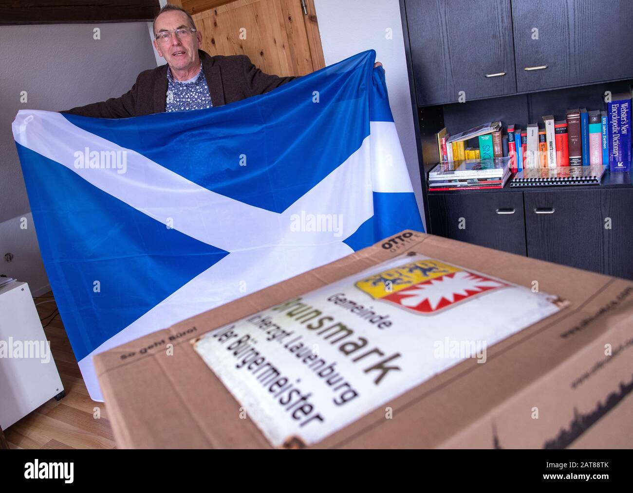 Brunsmark, Allemagne. 31 janvier 2020. Iain Macnab, maire de la petite communauté de Brunsmark près de Mölln, montre un drapeau de l'Ecosse sur son dernier jour de travail, qu'il a reçu comme cadeau d'adieu. Sur le bureau il y a une boîte remplie de documents et le vieux signe du maire de la ville. L'Écosse vit en Allemagne depuis plus de quarante ans et est maire de la ville de 160 habitants depuis onze ans. Avec la brexite Macnab doit démissionner de son bureau en tant que maire et n'est plus autorisé à participer au conseil municipal. Crédit: Jens Büttner/Dpa-Zentralbild/Dpa/Alay Live News Banque D'Images