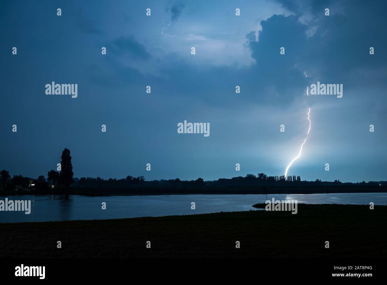 Éclair lumineux sans branches qui s'attaque à la terre près d'une rivière. Ce type de foudre est appelé 'foudre de canal de dent'. Banque D'Images