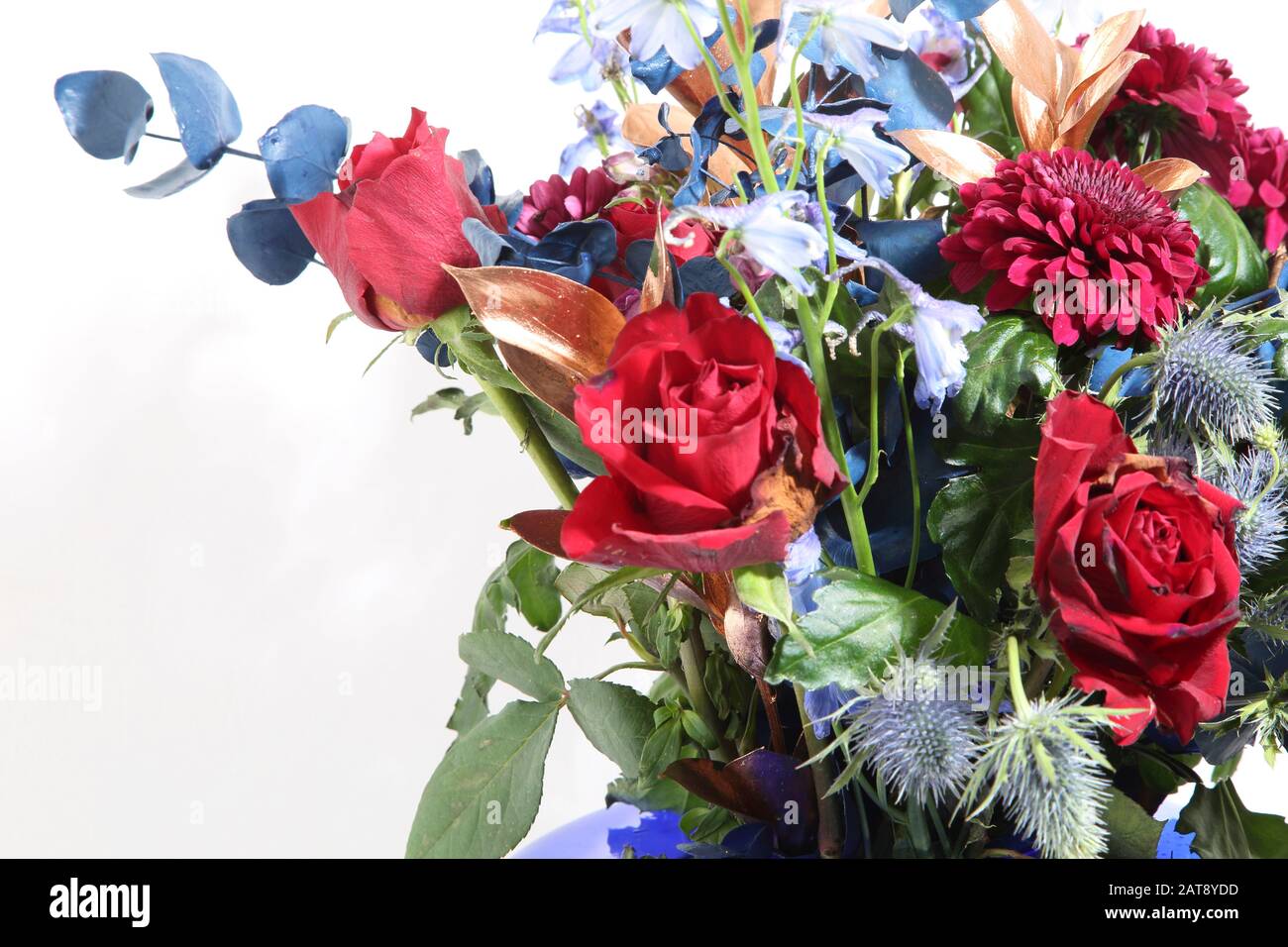 Un bouquet de roses, Eryngium Bourgatii et Chrysanthemums dans une vase en verre bleu Banque D'Images