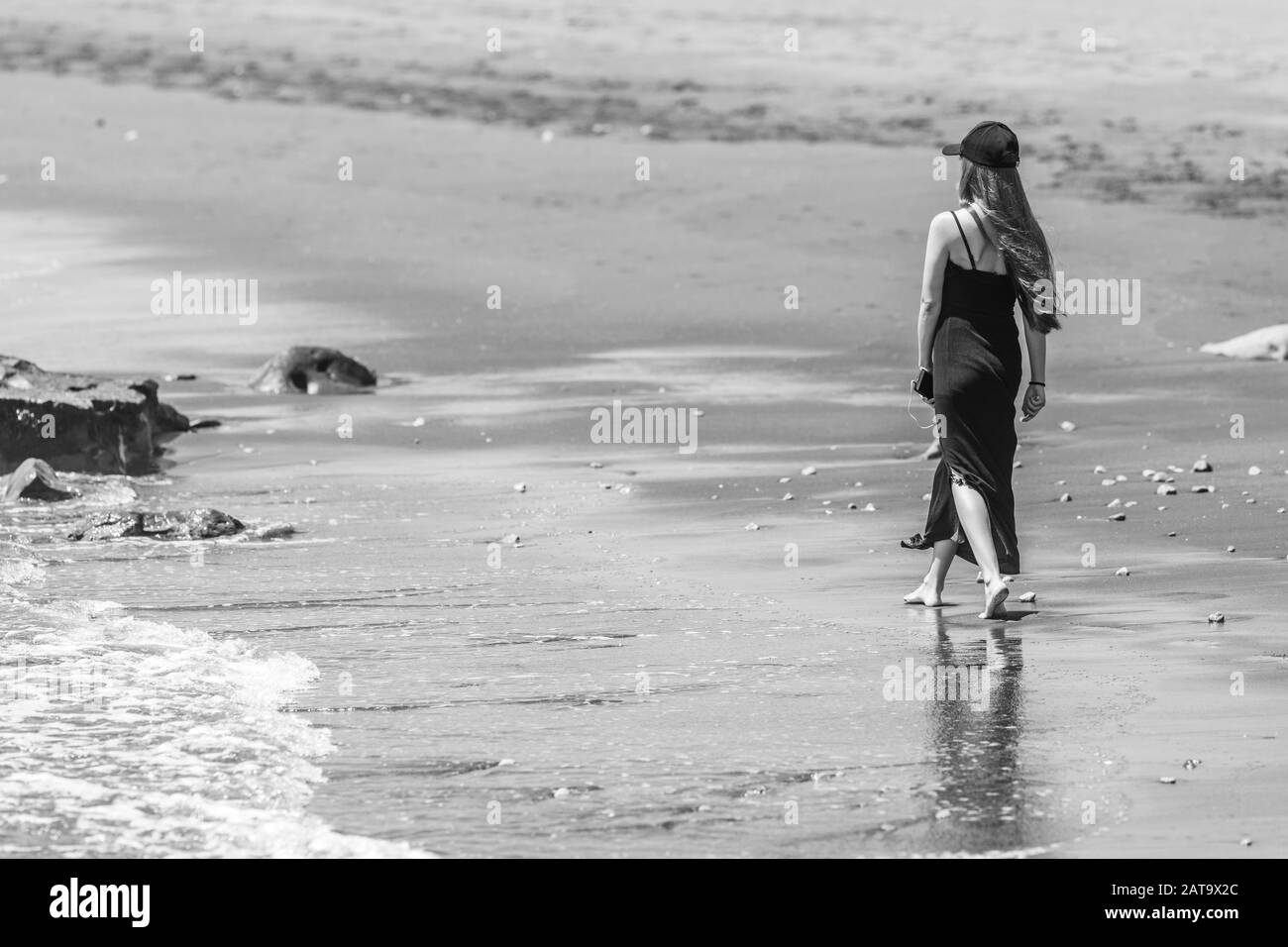 Jeune fille avec une robe noire et une hutte marchant sur la côte humide dans une plage à l'intérieur d'un paysage naturel impressionnant sur la côte chilienne. Profiter de vacances Banque D'Images
