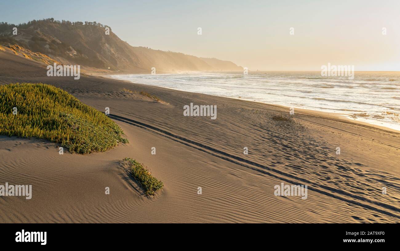 Magnifique coucher de soleil sur la vue sur l'eau de la côte chilienne. Un paysage de plage idyllique avec la lumière du soleil illuminant les dunes de sable avec des couleurs orange Banque D'Images