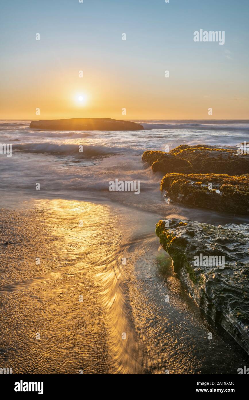 Une vue imprenable sur le coucher du soleil sur l'eau de la côte chilienne. Un paysage de plage idyllique avec la lumière du soleil illuminant les algues vertes et les rochers Banque D'Images