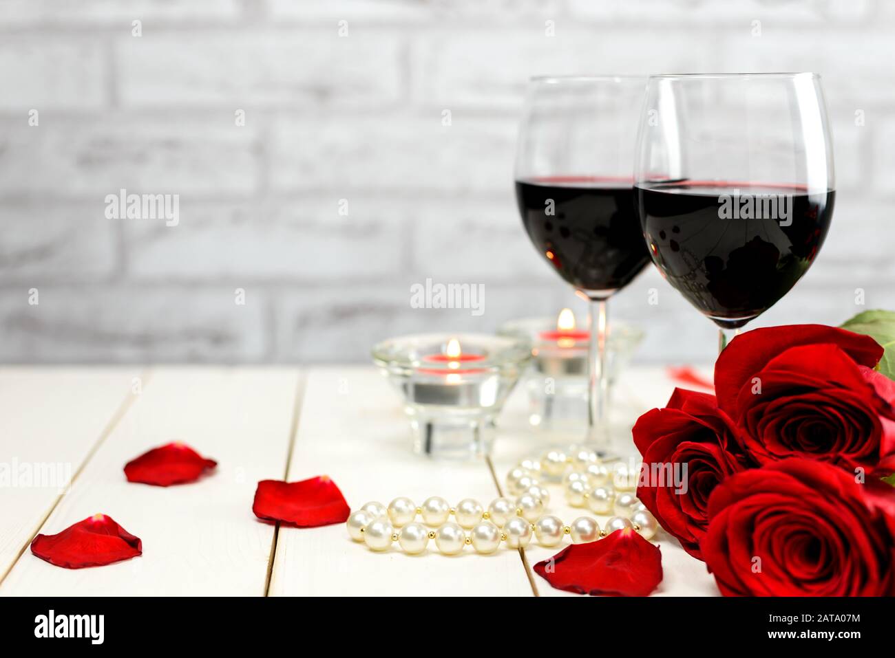 Concept Saint Valentin. Deux verres de vin, roses rouges, cordes de perles, pétales de roses et bougies brûlantes sur une table en bois blanc avec espace de copie pour Banque D'Images