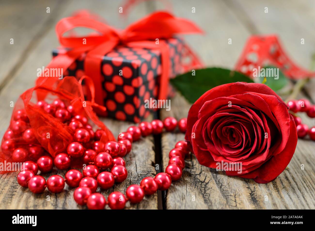Rose rouge, cordes de perles rouges et boîte cadeau sur une vieille table en bois. Mise au point sélective. Banque D'Images