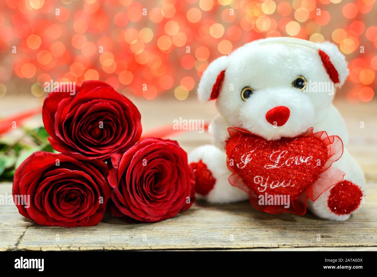 Concept de Saint Valentin. Ours en peluche blanc et roses rouges sur une vieille table en bois devant un fond lumineux flou. Mise au point sélective. Banque D'Images
