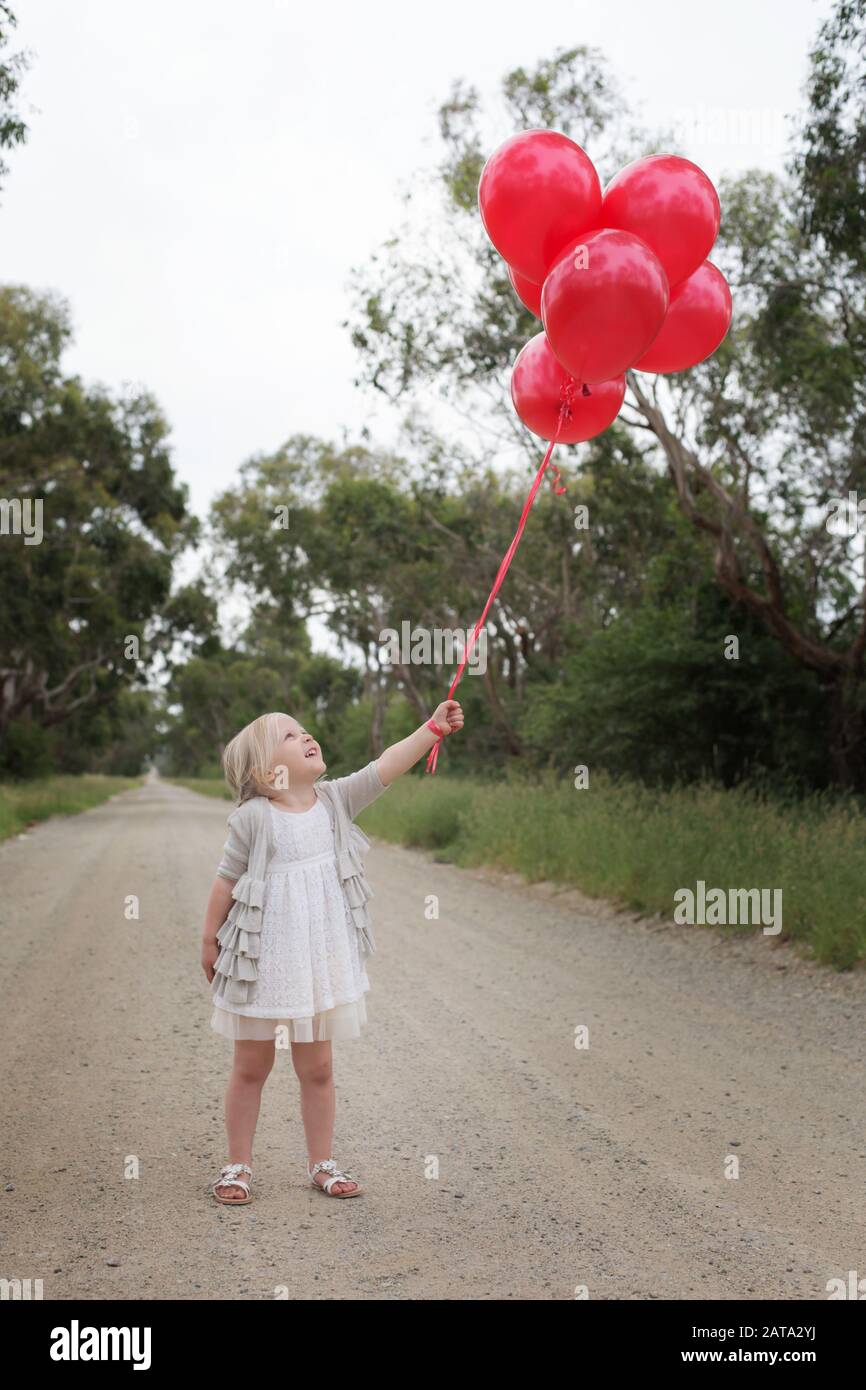 Fille australienne debout sur la route de terre tenant des ballons rouges et les regardant vers le haut Banque D'Images