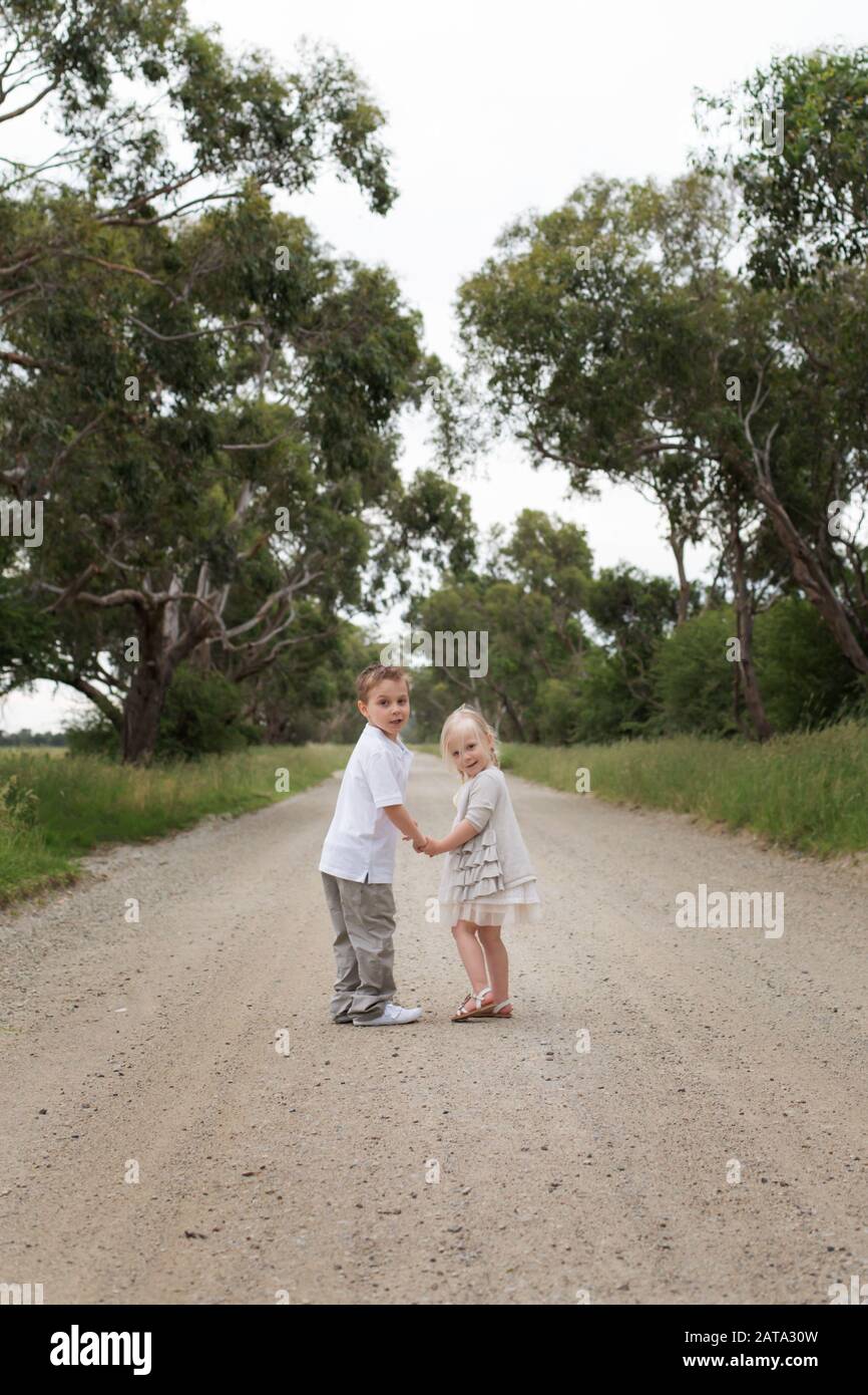 Australien garçon et fille tenant les mains tout en se tenant sur la route de terre, regardant en arrière à l'appareil photo Banque D'Images