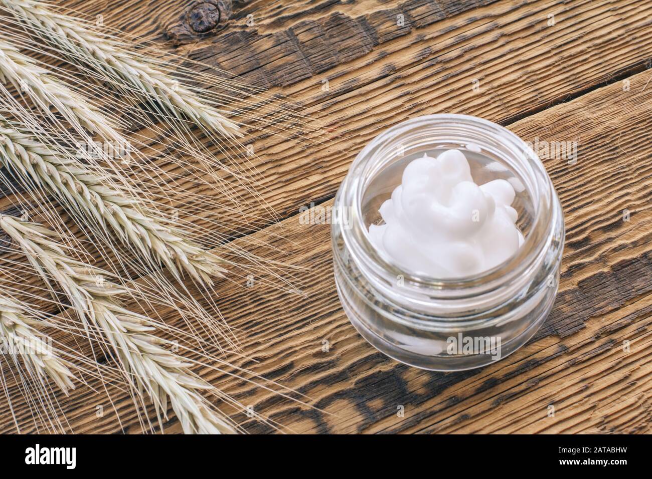 Crème cosmétique dans un bocal en verre et spiquets secs de blé sur de vieilles planches en bois. Vue de dessus. Banque D'Images