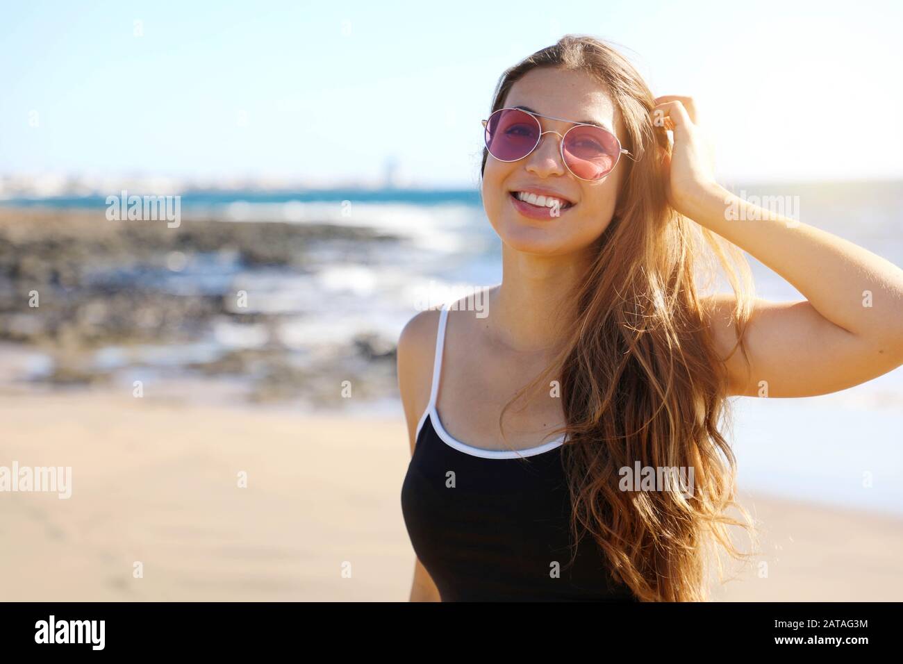 Jolie femme sportive moderne avec des lunettes de soleil souriant heureux à  l'appareil photo sur la plage Photo Stock - Alamy