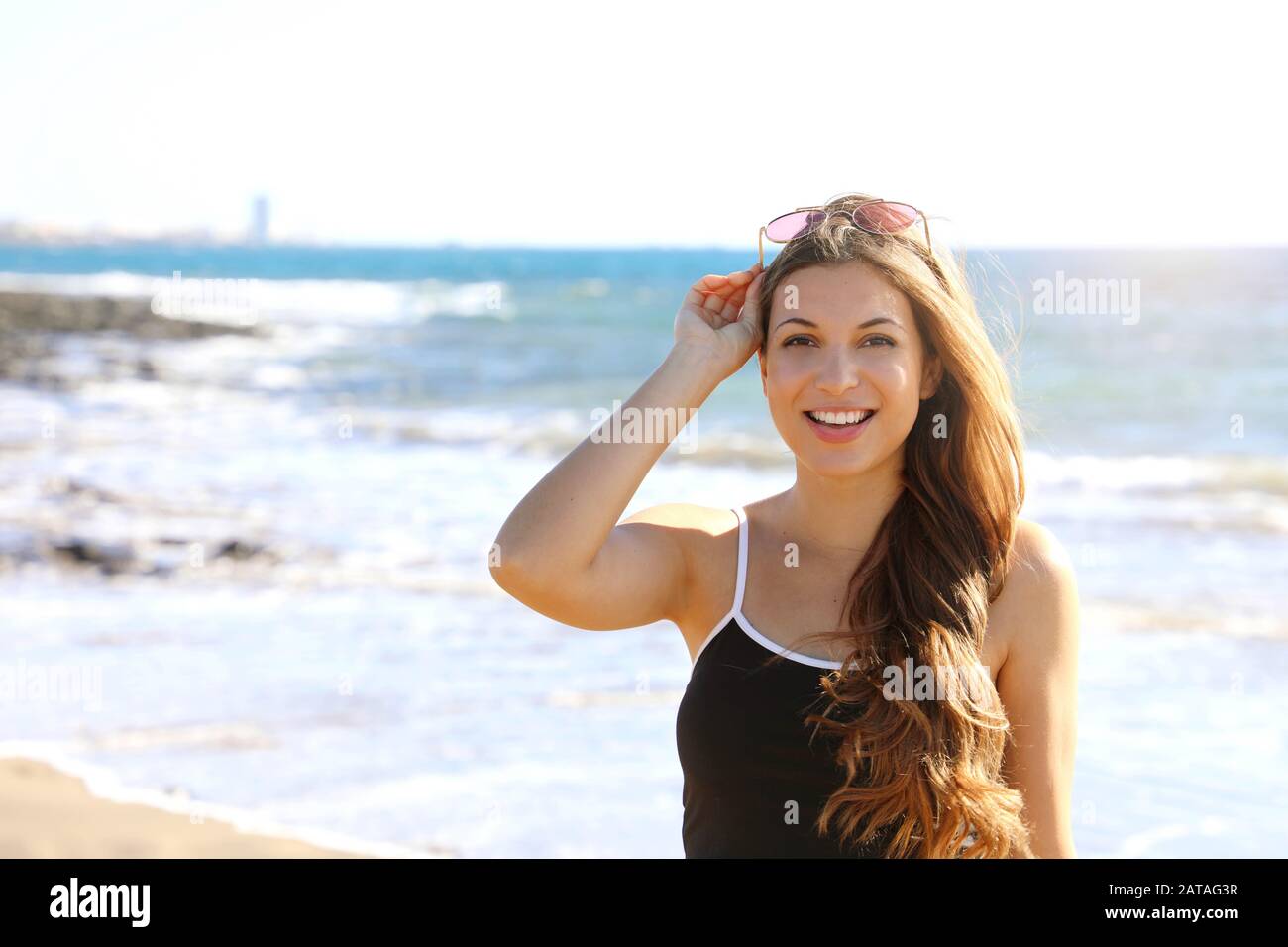 Jolie femme sportive moderne avec des lunettes de soleil sur sa tête regardant sourire heureux à l'appareil photo sur la plage Banque D'Images