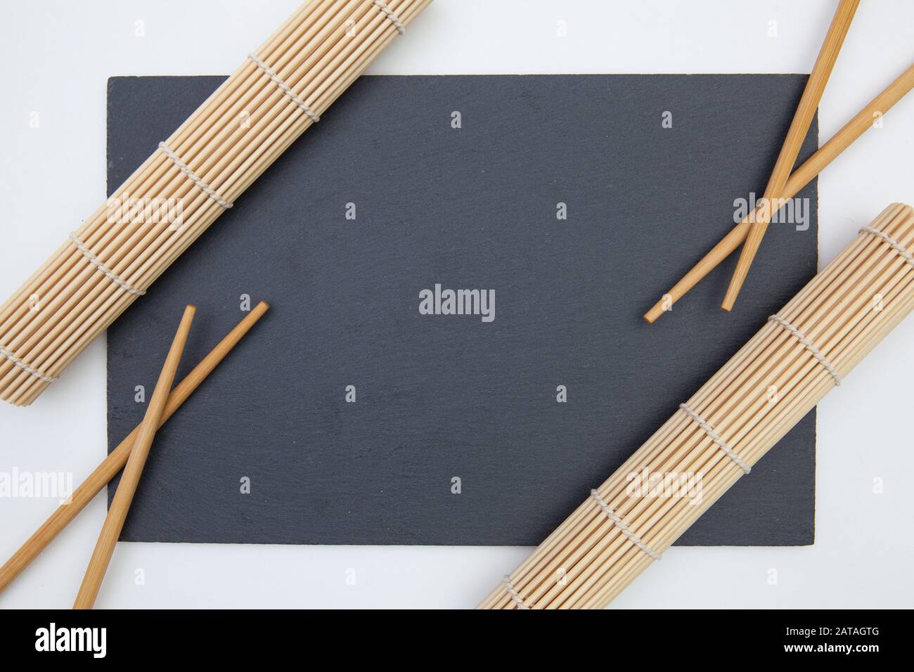 Plaque rectangulaire en ardoise avec baguettes, tapis en bambou pour sushi sur la table blanche. Conception Alimentaire Banque D'Images