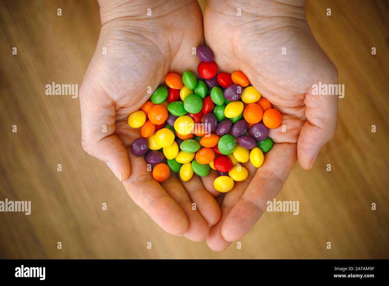 Tambov, Fédération de Russie - 05 décembre 2019 bonbons aux fruits multicolores Skittles dans les mains des femmes. Fond en bois. Banque D'Images