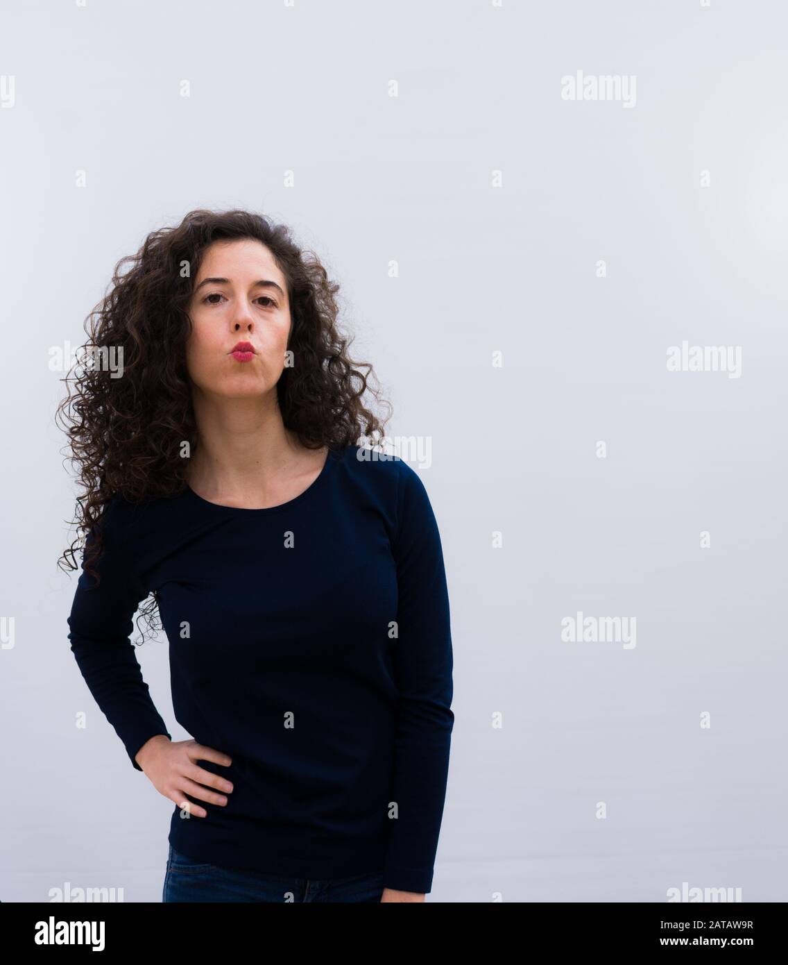 jeune jolie femme avec des cheveux bouclés noirs et des lèvres avec un mignon, amusant, heureux, belle expression, envoyant un baiser contre le mur blanc Banque D'Images