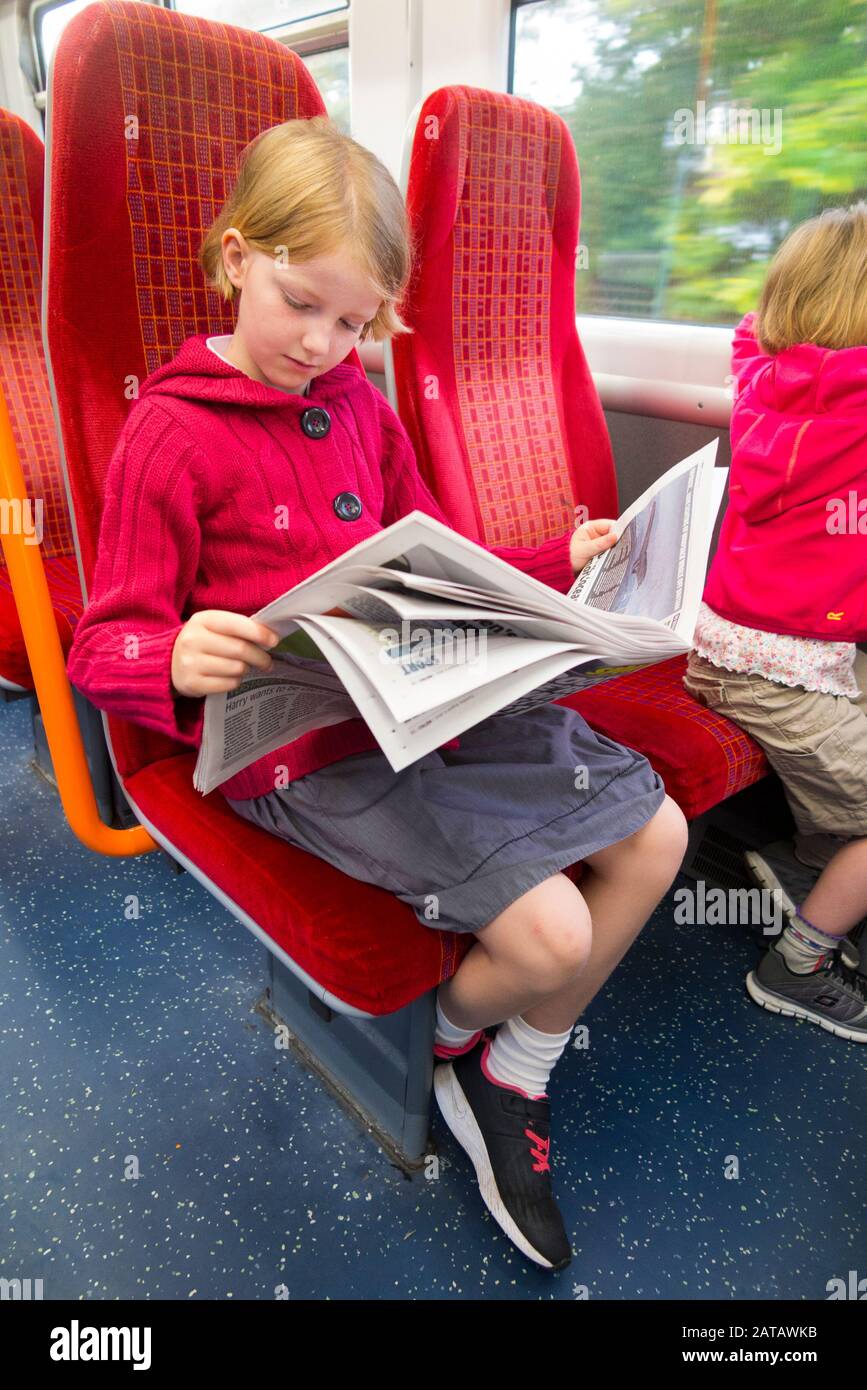 Assis fille de neuf ans enfant / enfant / enfants lisant un journal du matin / papier gratuit tout en étant assis sur le train à Londres Royaume-Uni Angleterre Royaume-Uni. (112) Banque D'Images