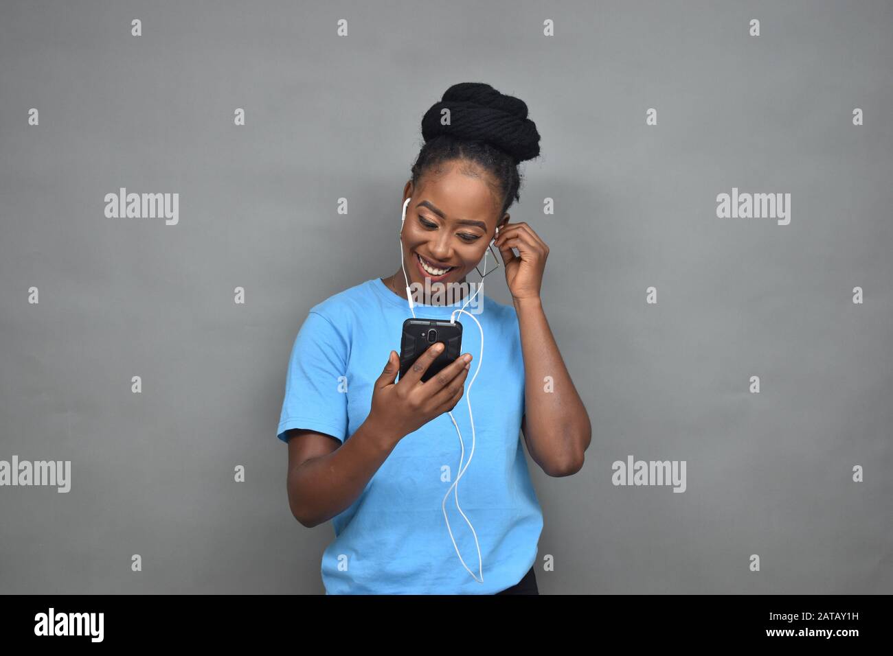 jolie jeune femme noire souriante tout en écoutant de la musique et en utilisant son téléphone portable pour discuter, envoyer des sms, naviguer Banque D'Images