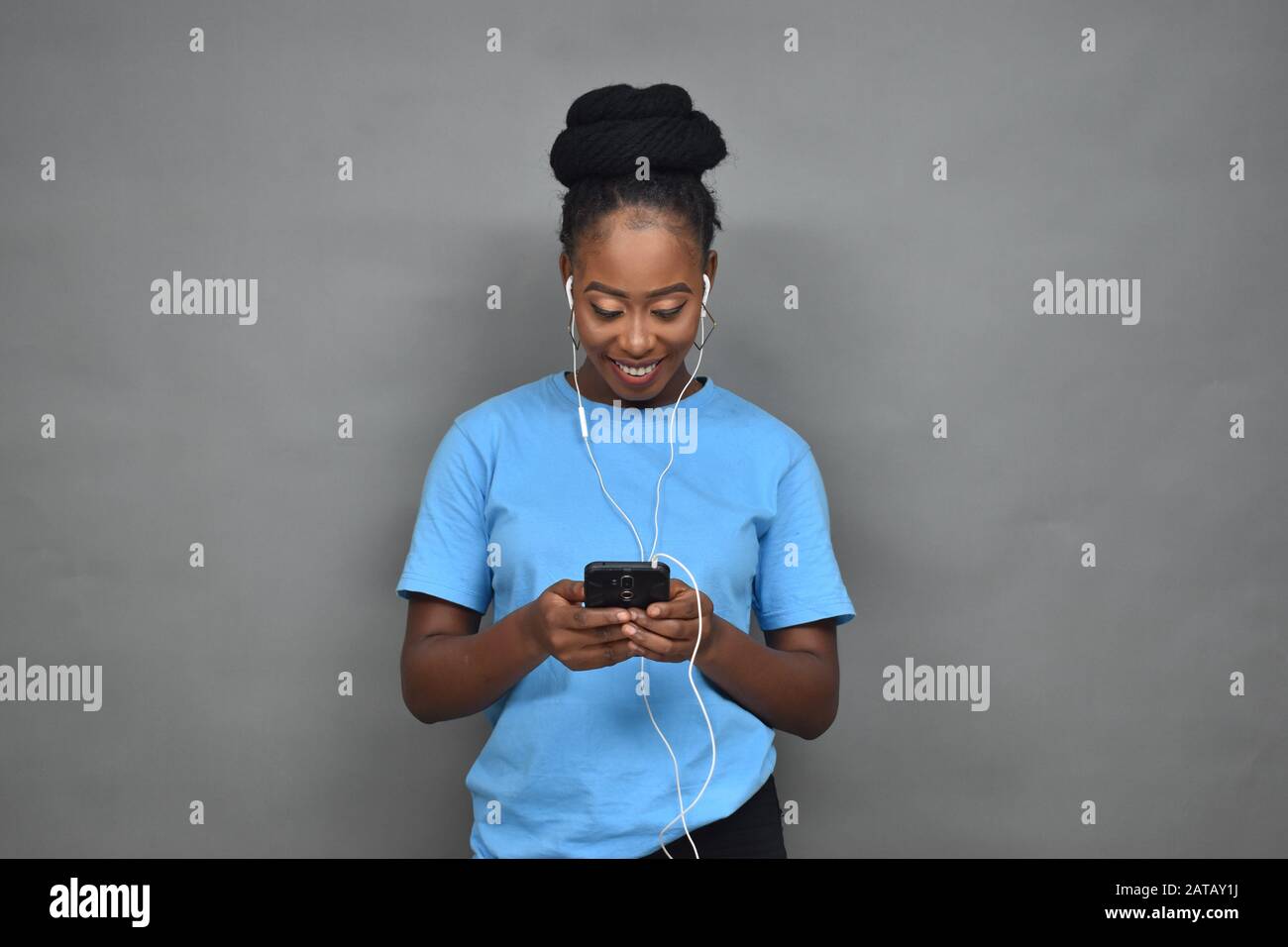jolie femme noire souriante tout en écoutant de la musique et en utilisant son téléphone portable pour discuter, envoyer des sms, naviguer Banque D'Images