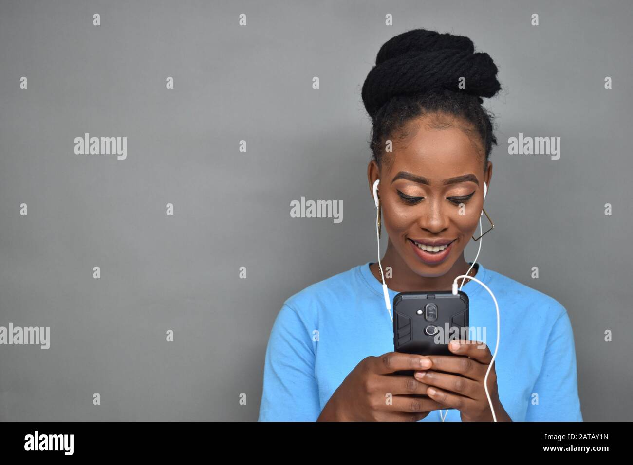 belle fille noire souriant tout en écoutant de la musique et en utilisant son téléphone portable pour discuter, envoyer des sms, naviguer Banque D'Images