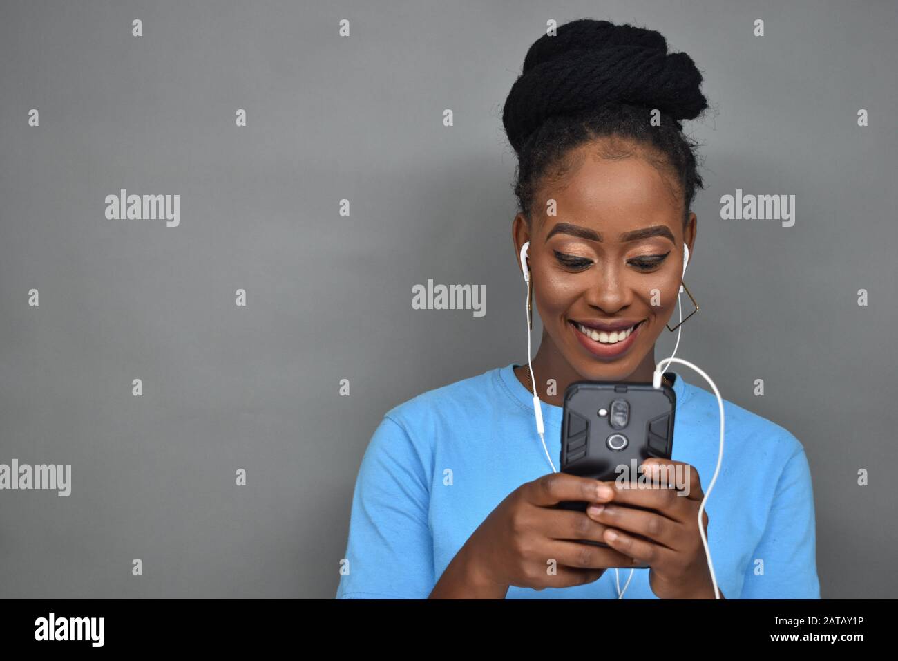 jolie dame noire souriante tout en écoutant de la musique et aussi en utilisant son téléphone portable pour discuter, envoyer des sms, naviguer Banque D'Images