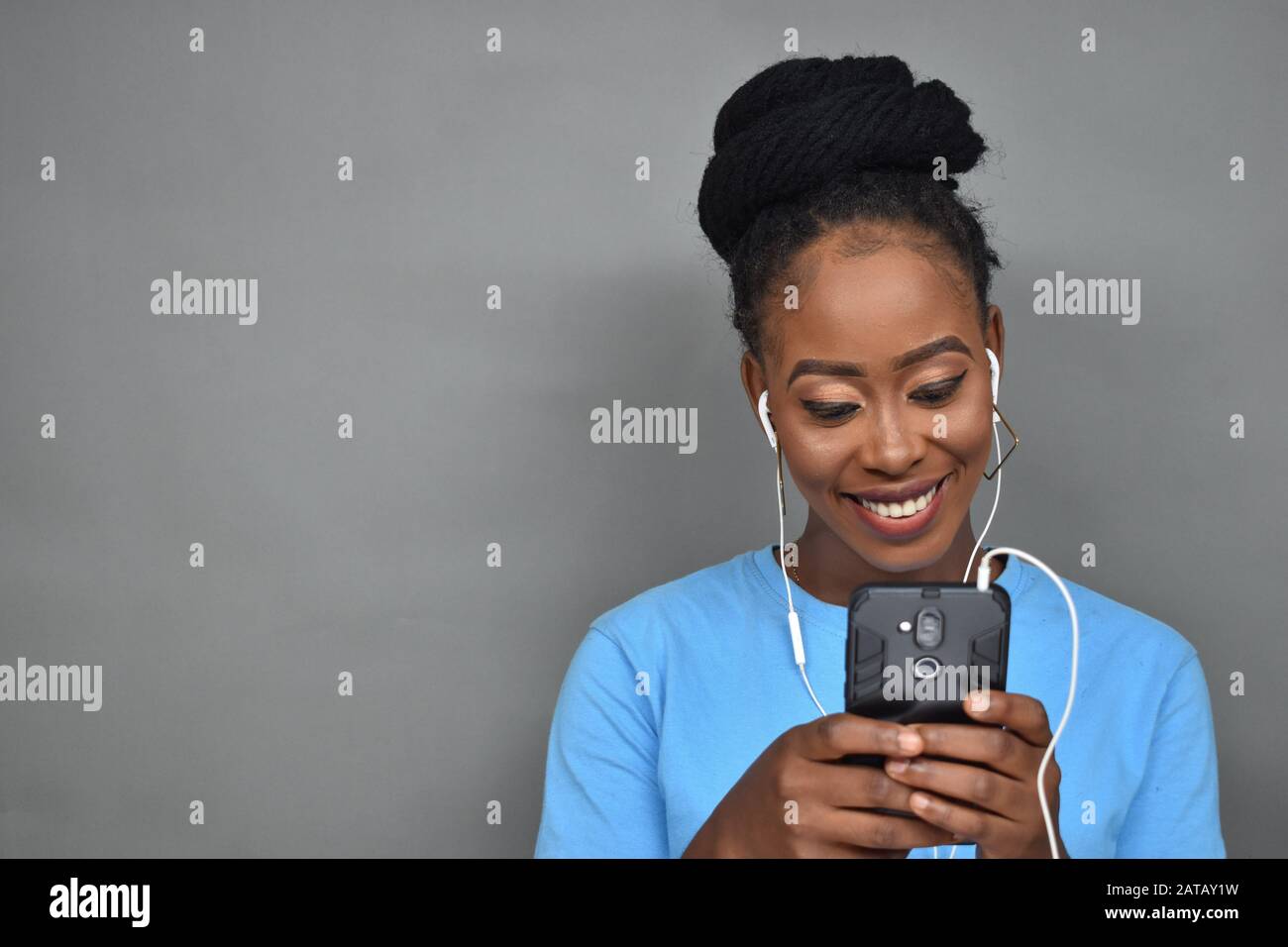 belle dame noire souriante tout en écoutant de la musique et aussi en utilisant son téléphone portable pour discuter, envoyer des sms, naviguer Banque D'Images