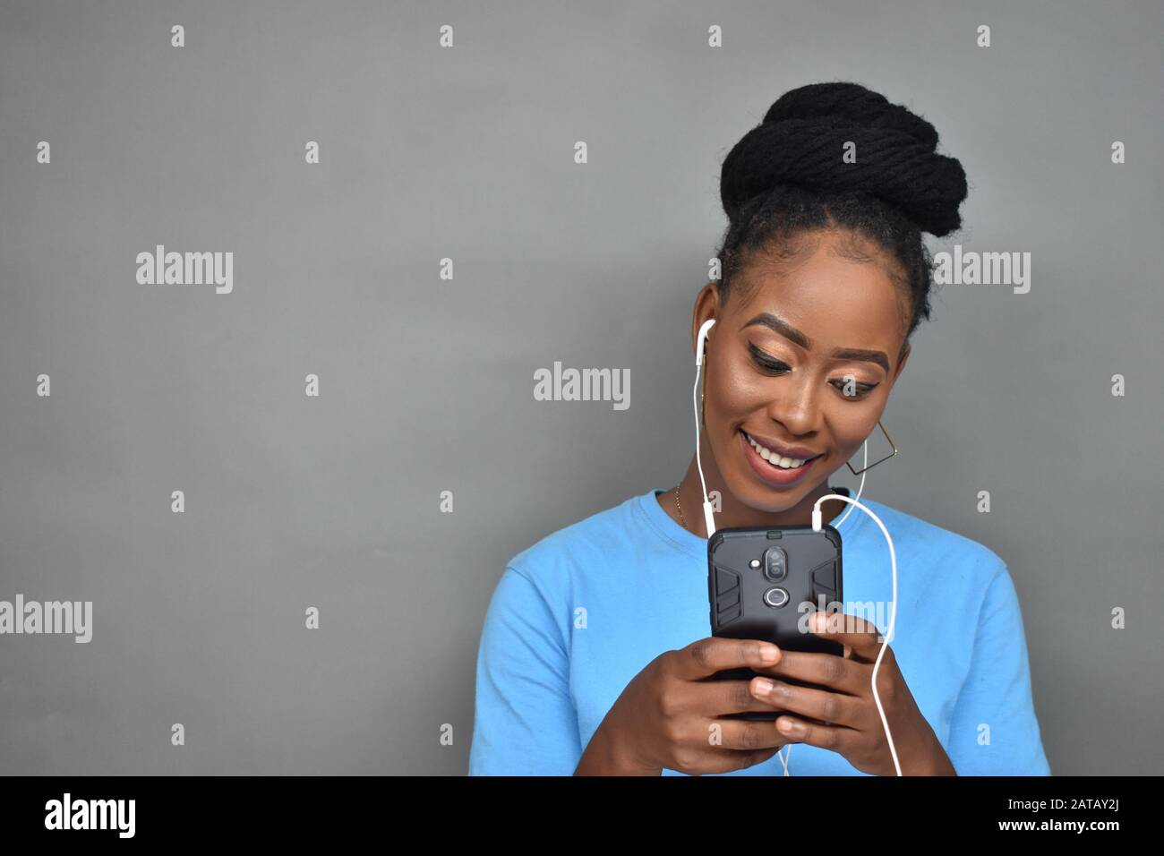 belle femme noire souriant tout en écoutant de la musique et en utilisant son téléphone portable pour discuter, envoyer des sms, naviguer Banque D'Images