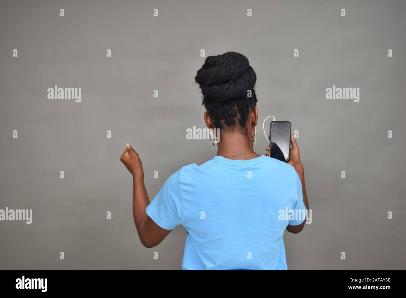 belle femme africaine à écouter de la musique et aussi à regarder du contenu sur son téléphone mobile se sentant excitée, vue arrière Banque D'Images