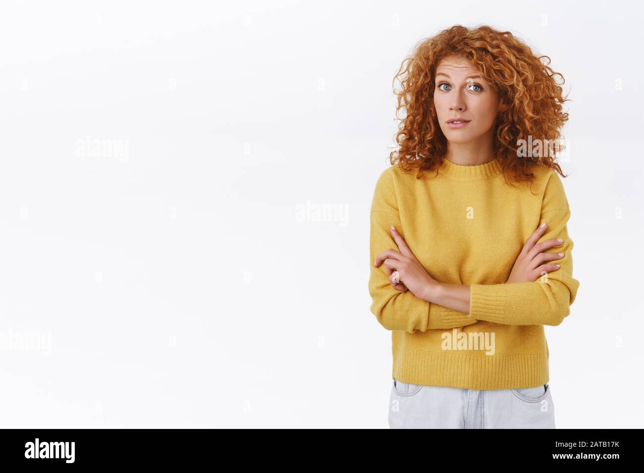 Sceptique jolie tête rouge femelle dans le chandail jaune, avec les cheveux frisés, la poitrine de bras croisés, soulever les sourcils et la caméra de stare avec incrédulité, écouter quelqu'un Banque D'Images